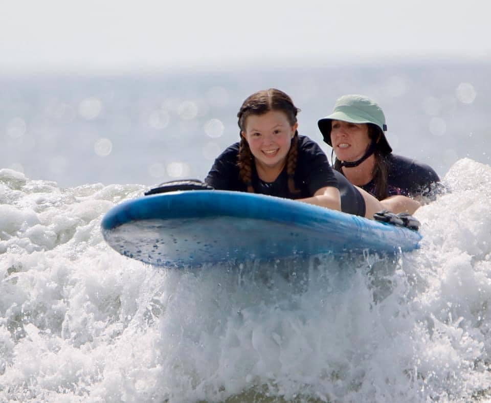 A young person in the water on an adaptive surfboard with a volunteer