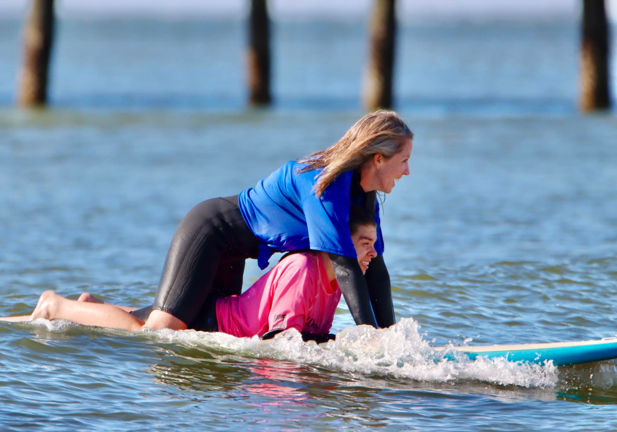 A young person and a volunteer riding a surfboard